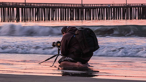 A commercial photographer kneeling in the ocean waves at Avila Beach