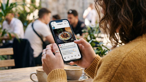 A woman looking at her phone interacting with social media post while sitting at busy cafe
